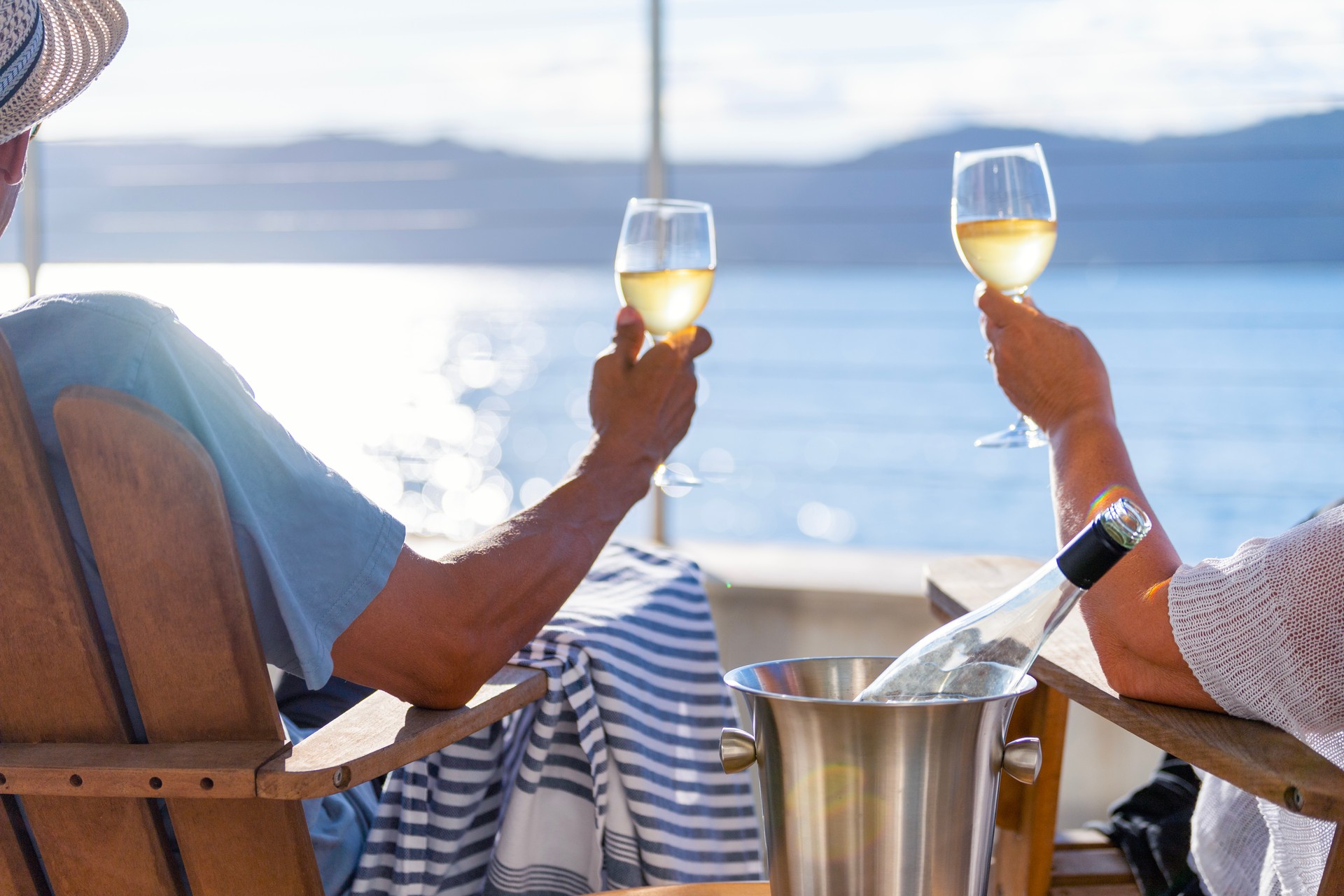 Couple relaxing and drinking wine on deck chairs in an over water bungalow.